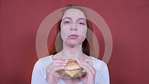 Woman eating a hamburger on red background. Fast food eats