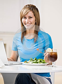 Woman eating healthy lunch while typing on laptop