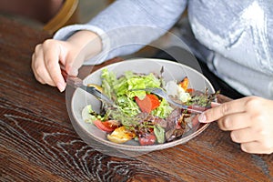 Woman is eating healthy vegetables and beef salad with knife and fork on wooden table