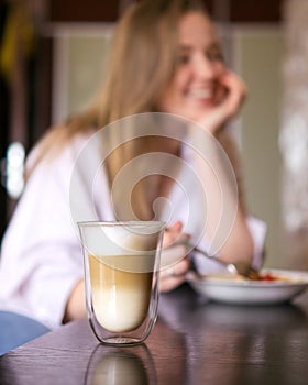 Woman eating her breakfast and drinking coffee while sitting at the table. Focus on the latte
