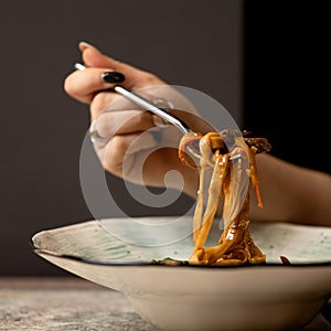 Woman eating hot pasta with fork. Italian food, noodles or spaghetti with tomato sauce on blured background. Food plate