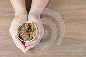 Woman eating Insects Silkworm Pupae Bombyx Mori. Her hand holding disposable cup which containing worm snack deep-fried for take