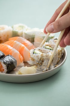 Woman eating Japanese tuna avocado inside out California with salmon Nigiri and Maki from sushi mix plate with wooden chopsticks