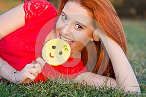 Woman eating a lollipop and smiling lying on green grass lawn