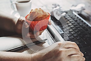 Woman eating muffin at workplace. Unhealthy snack