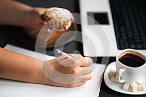 Woman eating muffin at workplace. Unhealthy snack