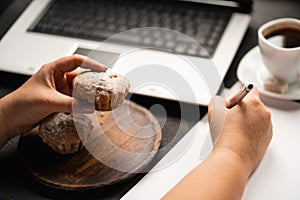 Woman eating muffin at workplace. Unhealthy snack