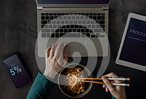 Woman Eating Noodle while Working on Computer Laptop, Mobile Phone and Tablet. Top View. Unhealthy Food in a Busy Working Day