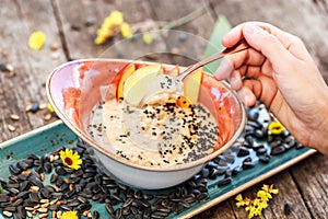 Woman eating oatmeal porridge sunflower seeds, sesame and peaches. Selective focus.