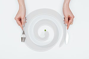 Woman eating one small green pea using knife and fork