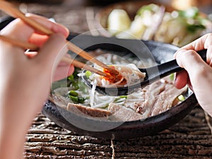 Woman eating pho with sriracha using chopsticks and spoon together