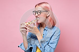 Woman eating a piece of pizza against a pink background