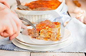 Woman eating piece of tasty hot lasagna served on a white plate. Italian cuisine, menu, recipe. Homemade meat lasagna. Close up,