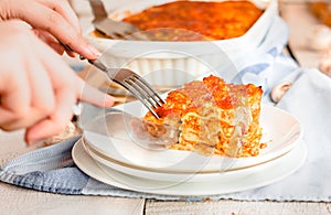 Woman eating piece of tasty hot lasagna served on a white plate. Italian cuisine, menu, recipe. Homemade meat lasagna. Close up,