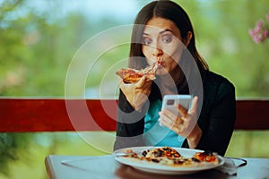 Woman Eating a Pizza while Checking her Phone photo