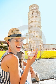 Woman eating pizza in front of tower of Pisa