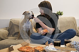 A woman eating pizza at home and sharing a bite with her dog.