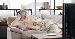 Woman eating popcorn and watching tv with disinterest