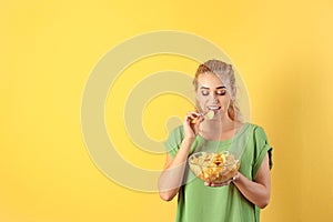 Woman eating potato chips on color background.
