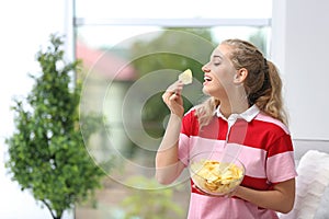 Woman eating potato chips in living room.