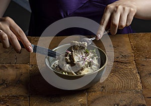 Woman eating rack of lamb in cream sauce with apple and radish in a bowl .