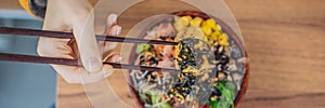 Woman eating Raw Organic Poke Bowl with Rice and Veggies close-up on the table. Top view from above horizontal BANNER