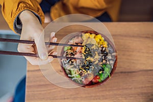 Woman eating Raw Organic Poke Bowl with Rice and Veggies close-up on the table. Top view from above horizontal