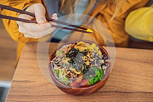 Woman eating Raw Organic Poke Bowl with Rice and Veggies close-up on the table. Top view from above horizontal