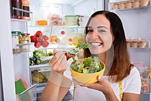 Woman Eating Salad In Front Of Refrigerator