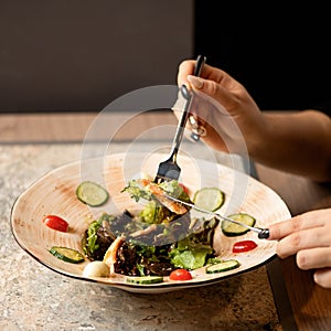 Woman eating salad with knife and fork. Close-up shot of female hands with cutlery and clay plate with greens and