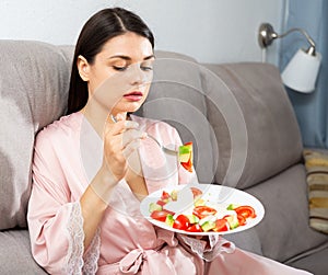 Woman eating salad on sofa
