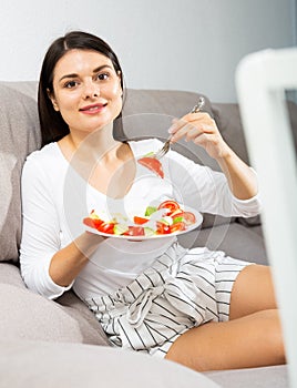 Woman eating salad on sofa