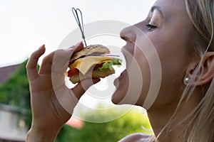 Woman eating sandwich. She opened her mouth, holding a hamburger on his outstretched hands and closed her eyes.