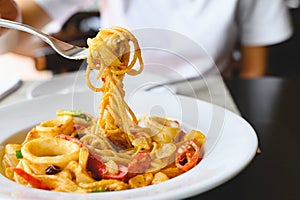 Woman eating seafood spaghetti white sauce with a fork at Italian restaurant. Food and cuisine concept