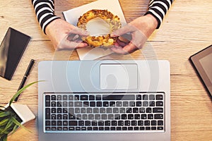 Woman eating sesame bagel for breakfast in office, top view