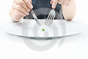 Woman eating a small green pea using knife and fork. Extreme weight loss diet concept