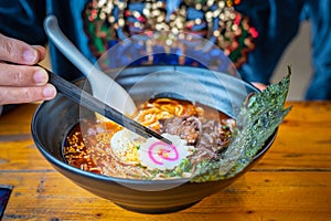 Woman eating a spicy ramen Japanese noodle soup in a black color ramen bowl