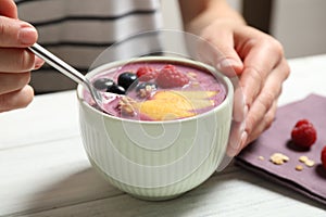 Woman eating tasty acai smoothie with fruits at white wooden table, closeup