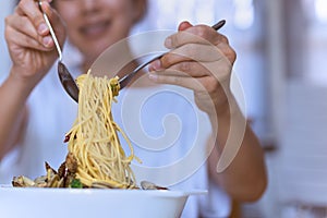 Woman eating tasty Italian spaghetti on white bowl with spoon and fork.