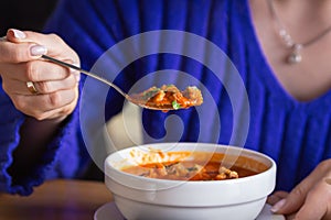 Woman eating tasty tomato soup gazpacho with croutons, vegetables and herbs in cafe. Hand holds a full spoon over a bowl