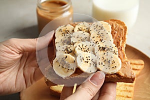 Woman eating toast with banana, peanut butter and chia seeds at table