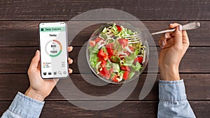 Woman eating vegetable salad and counting calories on mobile application