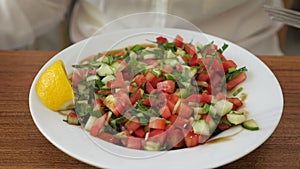 Woman is eating vegetable salad with lemon and greens, dish closeup.