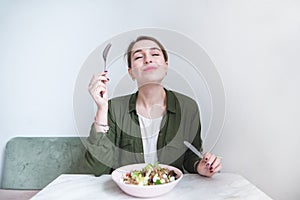 Woman eats a delicious salad. A sweet girl sits at the table, eats a plate salad and delights