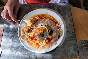 Woman eats homemade chicken cacciatore with pasta  and mushrooms in tomatoe sauce. Plate with chicken spagetti cacciatore on dinni