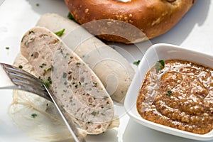 Woman eats Munich white sausage with knife and fork, sweet mustard and pretzel and take of sausage properly out of the gut