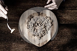 A woman eats nuts from a wooden tray in the shape of a heart. Wooden background. Shelled walnuts. Healthy eating