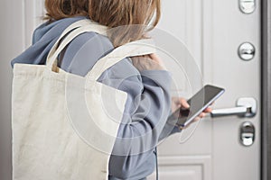 Woman with eco bag looking through shopping list on her phone before going to the store