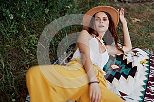 A woman in eco-friendly clothing in a hippie look is lying on a colored plaid smiling and looking at an autumn sunset in