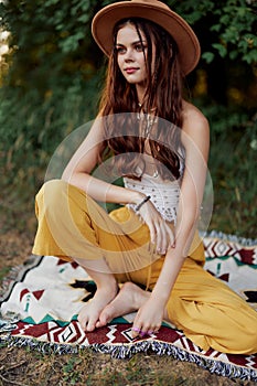 A woman in eco-friendly clothing in a hippie look is lying on a colored plaid smiling and looking at an autumn sunset in